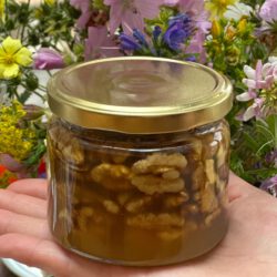 Eine Glas Walnüsse in Honig steht auf einer ausgestreckten Hand vor einem Strauß Wiesenblumen.